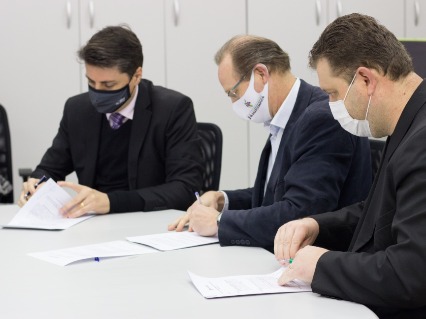 Three men sit and sign the paper at the same time.